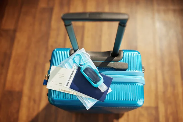 Travel during covid-19 pandemic. Upper view of trolley bag with sanitizer, medical mask and air ticket on the floor.