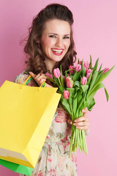 40歳の女性ともに長い波状ブルネットの髪でチューリップ花束とショッピングバッグにピンクの背景 — ストック写真