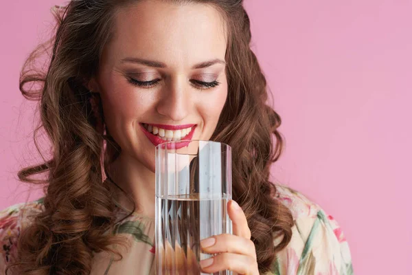 中年妇女面带微笑 一头长长的波浪般的黑发 杯中的水与粉色隔离 — 图库照片