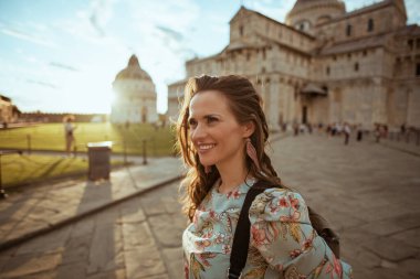 İtalya, Pisa 'daki Piazza Dei Mucizeleri' nde gezintiye çıkmış, çiçekli elbiseli, şık, yalnız bir turist kadın..