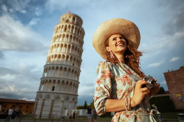 フィルムカメラとイタリアのピサの斜塔の近くの帽子を持つ花のドレスで若いソロ観光客の女性を笑顔 — ストック写真