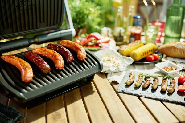 Summer backyard picnic. table with electric grill and grilled sausages.