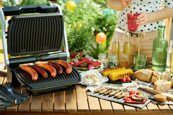 Summer backyard picnic. desk with electric grill and grilled sausages.