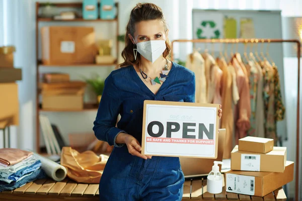 trendy small business owner woman with ffp2 mask, open after covid sign and antiseptic in the office.