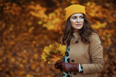 Merhaba Kasım ayı. Sonbahar sarı yapraklı kahverengi ceketli ve sarı şapkalı düşünceli kadın sonbaharda şehir parkında..