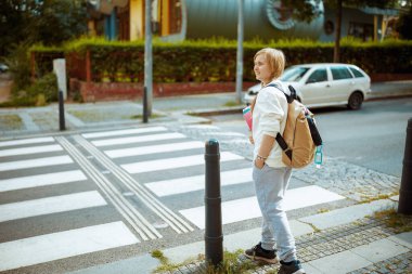 Beyaz tişörtlü, dezenfektan ve sırt çantalı şık bir çocuk yaya geçidinden geçip şehir dışındaki okula gidiyor..