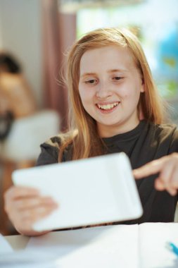 Gri tişörtlü, tabletli mutlu modern çocuk güneşli bir günde evde eğitim görüyor..