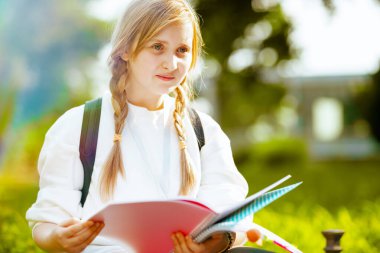 Şehirdeki çevre okulunun yanında iş kitabı ve sırt çantasıyla beyaz kazaklı, modaya uygun bir çocuk..