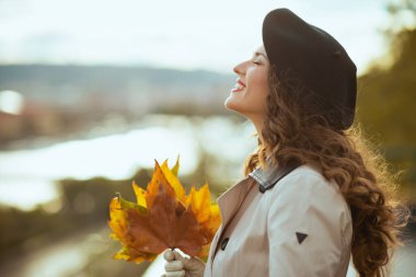 Merhaba Kasım ayı. Sonbaharda şehirde sonbahar sarısı yaprakları olan bej renkli trençkotlu orta yaşlı rahat bir kadın..