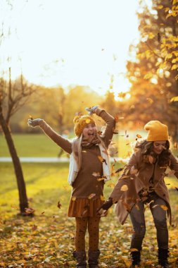 Merhaba Kasım ayı. Sarı şapkalı gülümseyen anne ve çocuk sonbaharda şehir parkında sonbahar yapraklarını kusar..