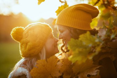 Merhaba Ekim. Sonbahar sarı yapraklı sarı şapkalı gülümseyen anne ve çocuk sonbaharda şehir parkında yaprakların arasında..