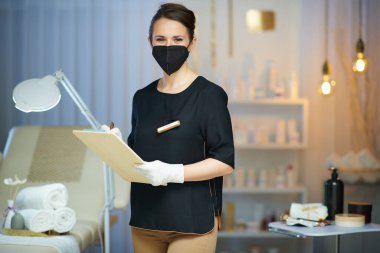 Koronavirüs salgını sırasında iş. Modern güzellik salonunda çalışan 40 yaşında, pano ve ffp2 maskeli bir kadın..