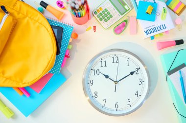 Okula dönelim. Çalışma kitapları, durağan, ders kitabı, saat ve sırt çantası olan beyaz masa güneşli bir günde öğrenci odasında..