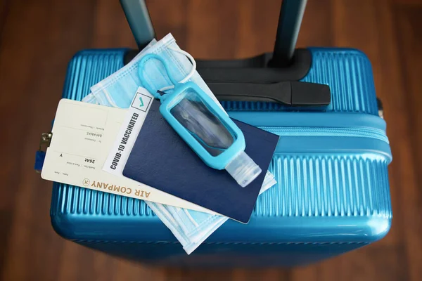 Travel during covid-19 pandemic. Closeup on trolley bag with antiseptic, medical mask and air ticket.