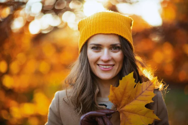 城市公园里身穿米黄色外套 头戴橙色帽子 头戴秋天黄色叶子的时髦女人在外面笑着 — 图库照片
