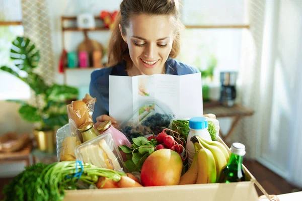 食品交付 中年妇女笑着 厨房里放着饭盒和菜谱 — 图库照片