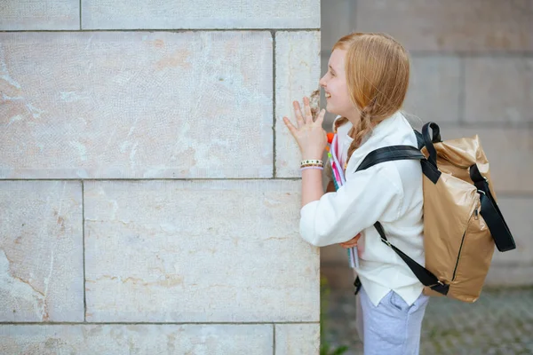 Smilende Stilfuld Pige Hvid Sweatshirt Med Arbejdsbog Rygsæk Mod Væg - Stock-foto