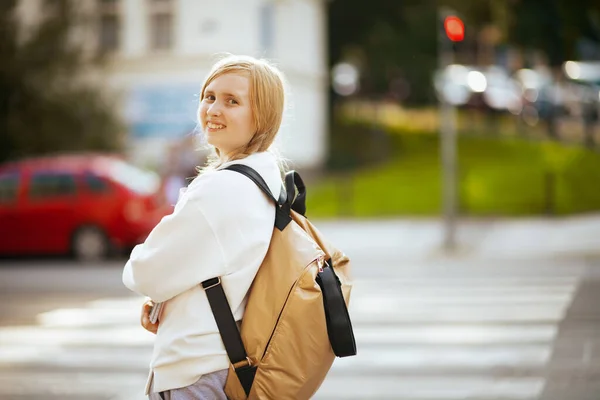 在城市里 穿着白色运动衫 背着背包 穿行在人行道上 走在户外上学的快乐的时髦女孩 — 图库照片