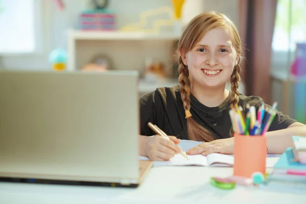 笑顔現代女子高生の肖像画でグレーシャツとノートパソコンとワークブックを持っています距離教育に自宅で晴れた日 — ストック写真