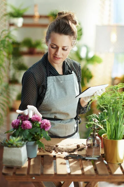 グリーン ホーム 現代中高年主婦で白いゴム手袋の鉢植え用タブレットPcを使用して現代の家で晴れた日 — ストック写真