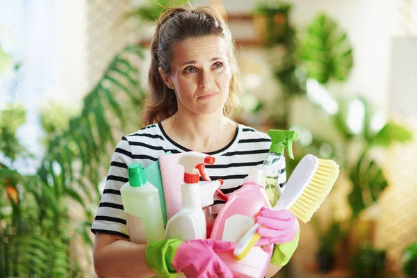 modern woman in striped shirt with cleaning supplies doing housework at modern home in sunny day.