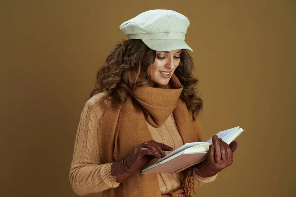 40岁身穿围巾 头戴皮手套 面带微笑的女人 阅读一本棕色背景的书 — 图库照片