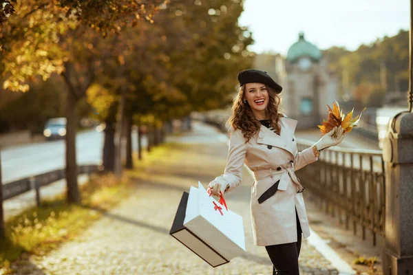 11月だ ショッピングバッグと秋の黄色の葉を持つベージュトレンチコートの幸せなスタイリッシュな女性秋に街の通りの外 — ストック写真