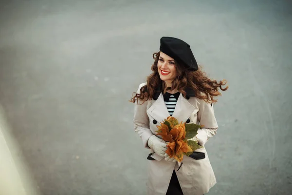 11月だ ベージュのトレンチコートを着た幸せな若い女性と秋に街の通りの外に黄色の葉と黒のベレー帽の上ビュー — ストック写真