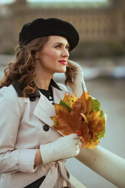 城市里穿着米黄色战壕外套 头戴黑色贝雷帽 头戴秋天黄色叶子的沉思型女性 — 图库照片