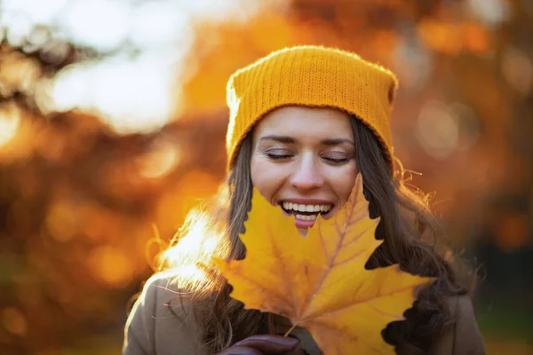 穿着米黄色外套 头戴橙色帽子 头戴秋天黄色叶子的快乐的年轻女子来到了城市公园 — 图库照片