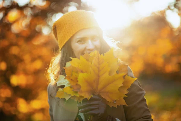 10月份 今年秋天 城市公园里 身穿米黄色外套 头戴橙色帽子 头戴秋天黄色叶子的40岁的时髦女人在外面笑着 — 图库照片