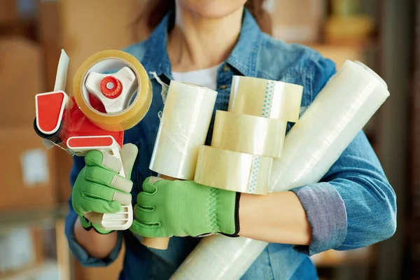 Delivery business. Closeup on female with packing tape dispenser, stretch wrap and adhesive tape in the office.