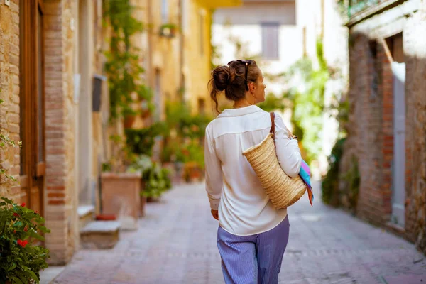 イタリア旅行 イタリアのトスカーナ州のピエンツァでウォーキングツアーをしているストローバッグを持つスタイリッシュな女性の後ろから見た — ストック写真