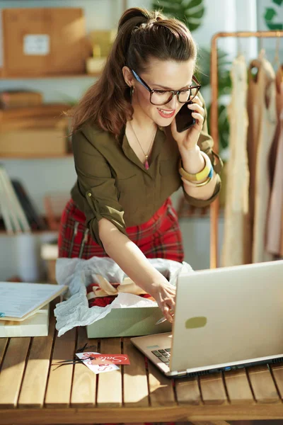 オフィスのスマートフォンでノートパソコンを話す幸せな若い中小企業経営者の女性 — ストック写真
