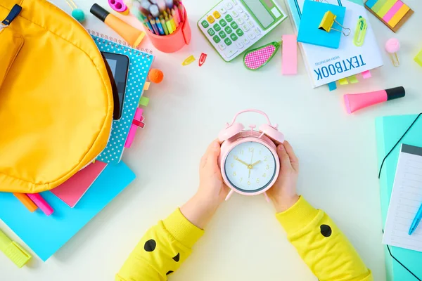 Back to school. Upper view of modern child with workbooks, stationary, textbook, clock and backpack at white table at home.