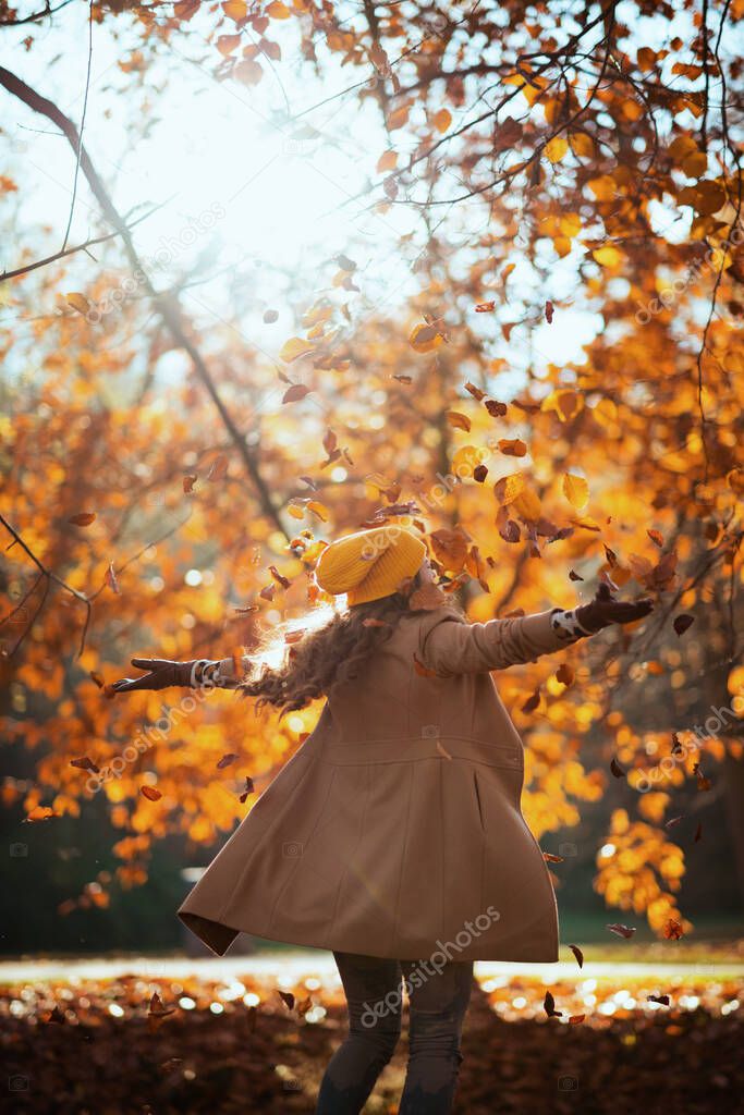 Hello autumn. smiling stylish woman in beige coat and orange hat rejoicing outdoors in the city park in autumn.