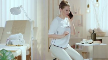 Modern güzellik salonunda akıllı telefondan konuşan gülen kadın çalışan..