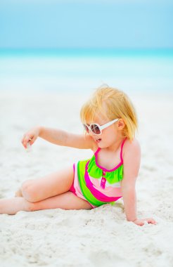 Kum ile kumsalda oynarken güneş gözlüklü kız bebek
