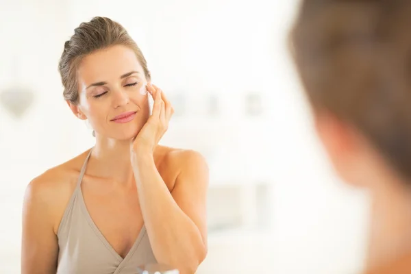 Happy young woman applying cream in bathroom — Stock Photo, Image