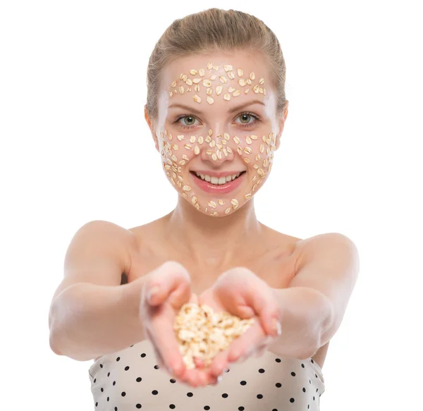 Mujer joven con mascarilla facial de avena que muestra avena — Foto de Stock