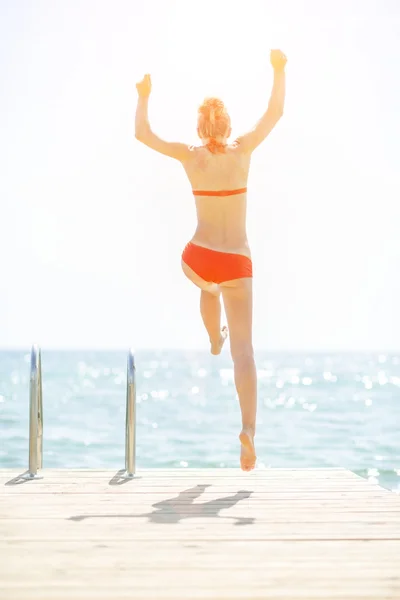 Junge Frau springt von Brücke ins Meer. Rückansicht — Stockfoto