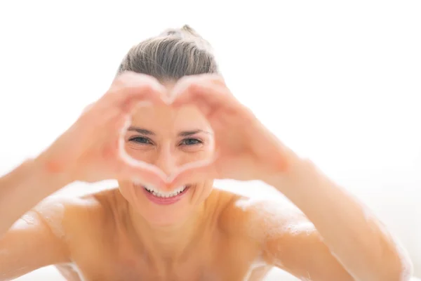 Mujer joven en bañera mirando a través de las manos en forma de corazón — Foto de Stock