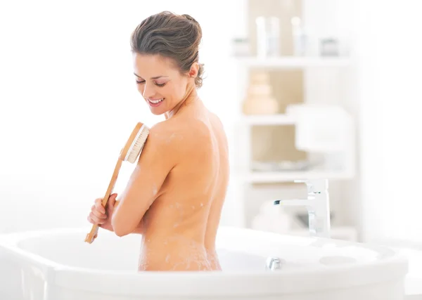 Mujer joven usando cepillo corporal en la bañera — Foto de Stock
