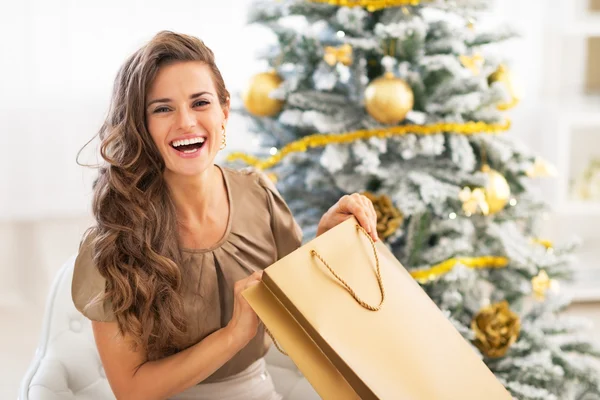 Happy young woman opening shopping bag near christmas tree — Stock Photo, Image