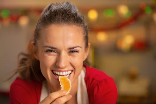 Portrait of young housewife eating orange in christmas decorated — Stock Photo, Image