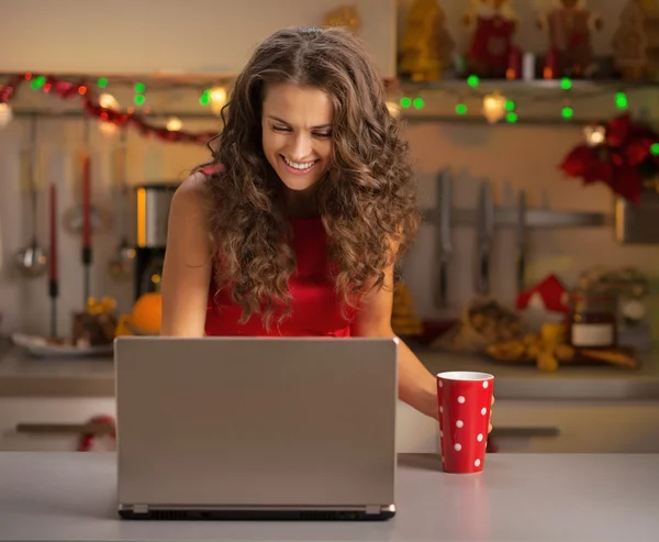 Glückliche junge Hausfrau mit Tasse heißer Schokolade mit Laptop in — Stockfoto