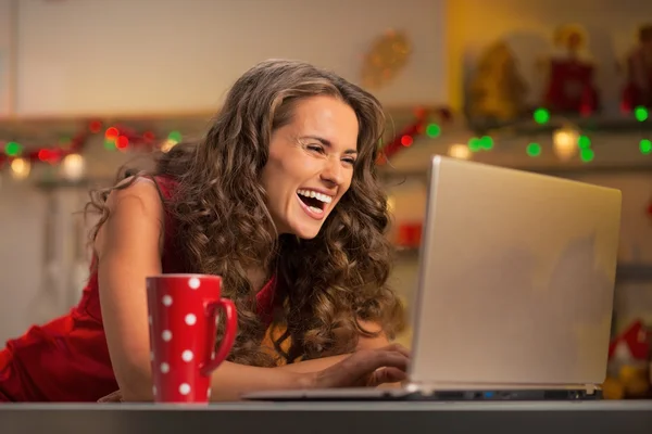 Glückliche junge Hausfrau mit Tasse heißer Schokolade mit Laptop in — Stockfoto