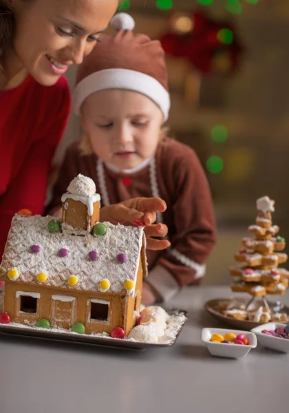 Happy mother and baby making christmas cookie house — Stock Photo, Image