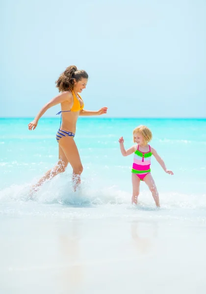 Mother and baby girl playing on sea shore — Zdjęcie stockowe