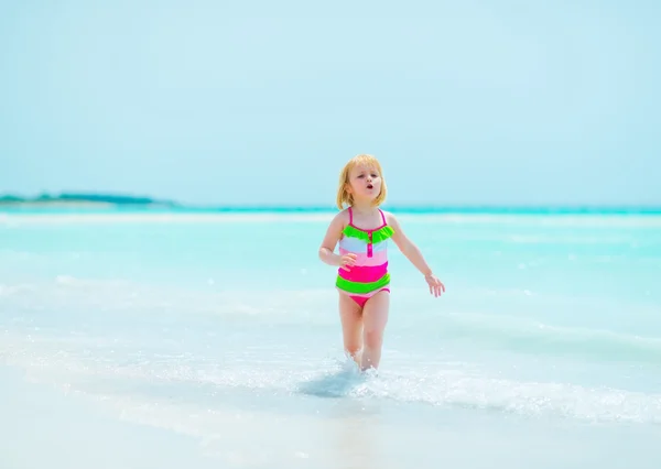 Baby girl running on sea shore — Stock Photo, Image